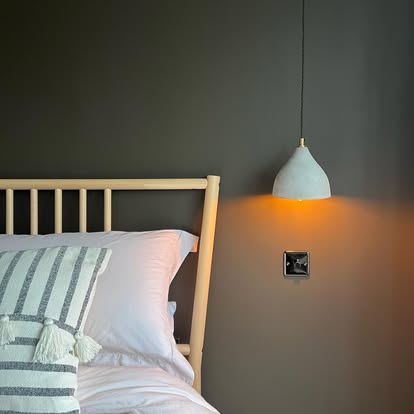 A bedroom with a pendant light and a dark faceplate on the wall