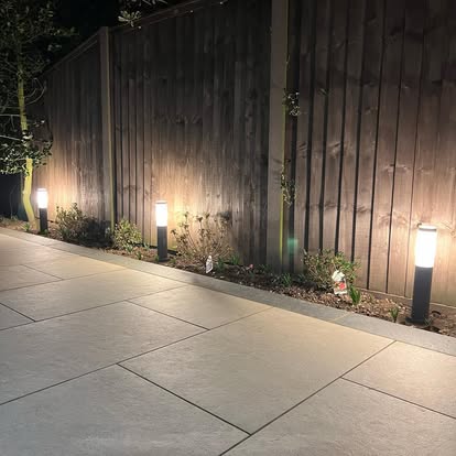 Bollard lights along a path beside a garden fence, at dusk