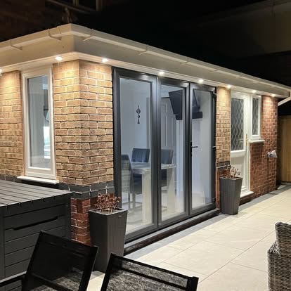 A brick extension with patio doors and lit soffit, at dusk