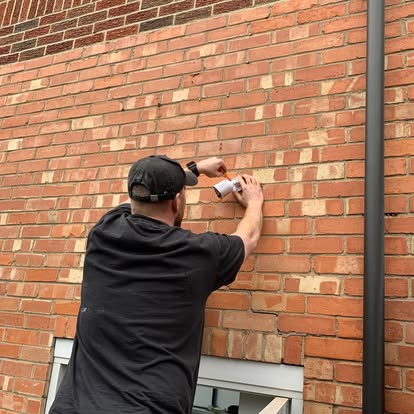 Tom Fryer screwing a small white fitting to a brick wall above a window