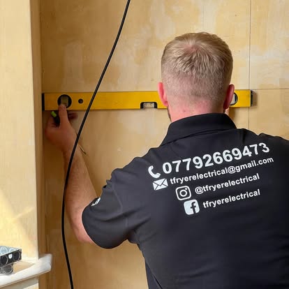 Tom Fryer holding a spirit level against a wall, in a branded polo printed with his number